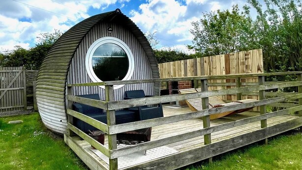 A wooden dome-shaped structure with a circular window, a wooden deck, and outdoor seating.