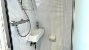 Un baño con cabina de ducha de vidrio, un lavabo blanco y un espejo.