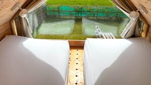 Una carpa con dos camas, vista a un campo verde y suelo de madera.