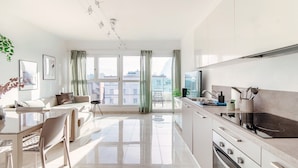 Une cuisine moderne dotée d’une grande fenêtre, un coin repas avec une table et des chaises, et un espace de vie avec un canapé et une table basse.