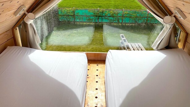 A tent with two beds, a view of a green field, and a ladder. - Lushna Petite 8 at Lee Wick Farm Glamping (Clacton on Sea)