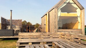 A wooden cabin with a triangular roof and a large window, surrounded by wooden pallets and construction materials. - Lushna Petite 8 at Lee Wick Farm Glamping (Clacton on Sea)