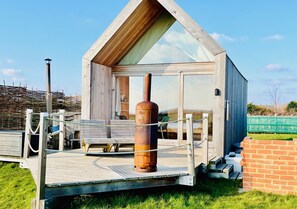 Una cabaña de madera con puerta de cristal, chimenea de metal y terraza de madera.