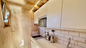A modern kitchen with wooden walls, white cabinets, a stainless steel sink, and a built-in toaster. - Lushna Petite 12 at Lee Wick Farm Glamping (Clacton on Sea)