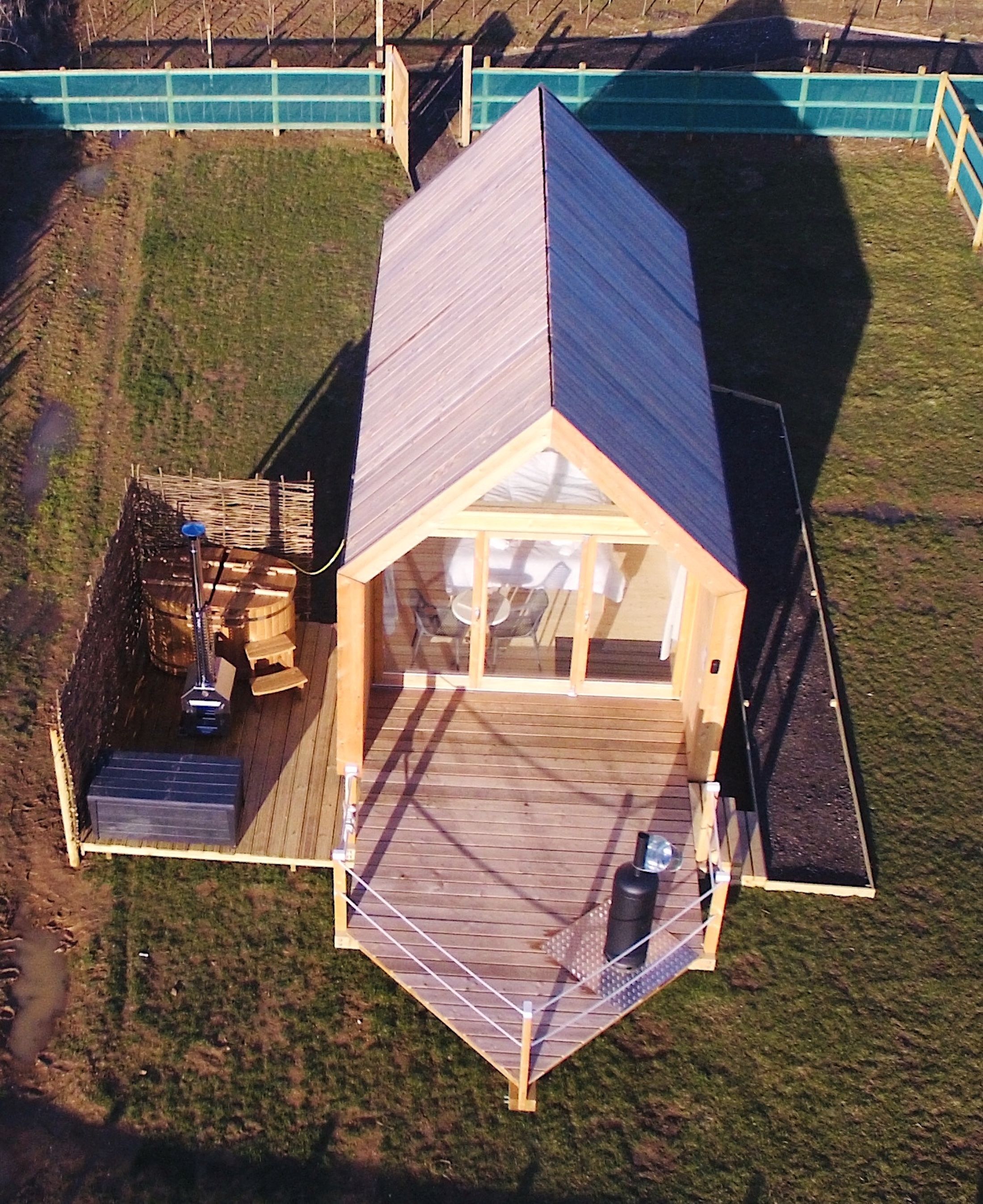 A wooden cabin with a deck, a small outdoor seating area, and a visible water feature.