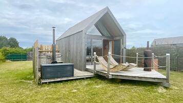 A modern outdoor structure with a glass door, a wooden deck, and a hot tub.