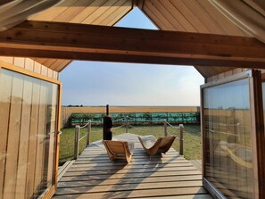 Un pontile in legno con due sedie e un tavolo vista spiaggia, con recinzione e vegetazione.