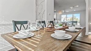 Un coin repas avec une table en bois dressée pour quatre personnes, comprenant des assiettes blanches, des bols et des verres à vin.
