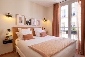 A hotel room with a large bed, two bedside tables, wall-mounted artwork, and a view of the outside through a sliding door. - Tinah Paris Aboukir (Paris)