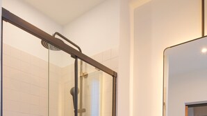 Ein modernes Badezimmer mit einer gläsernen Dusche, einem weißen Waschbecken und einem Spiegel darüber.