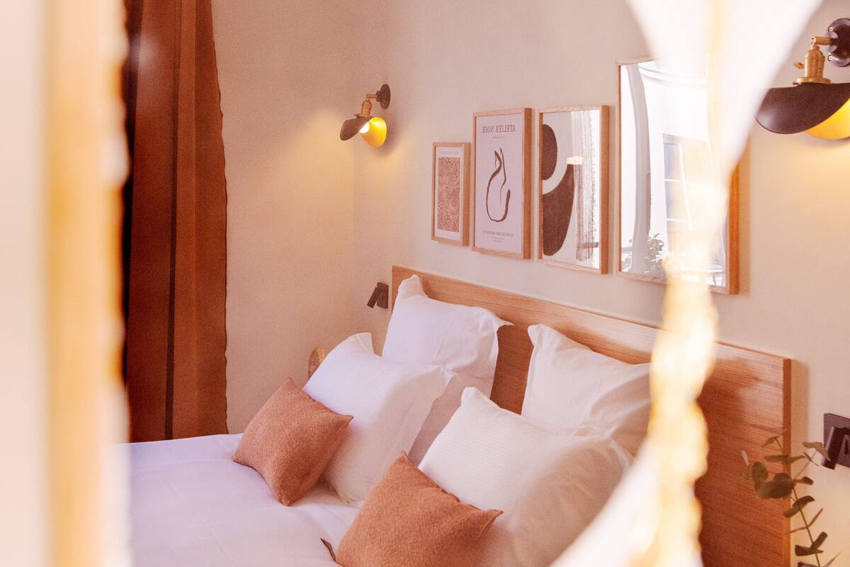 A neatly made bed with white and brown pillows, a wooden headboard, and framed artwork on the wall.