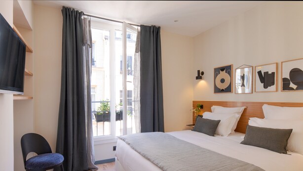 Ein Hotelzimmer mit Bett, Stuhl, Fenster mit Vorhängen und Wandbildern.
