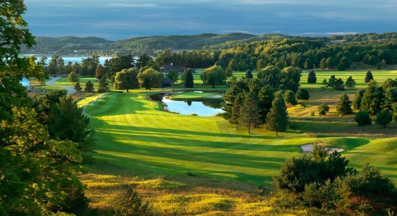 A golf course with a pond, trees, and a view of the surrounding landscape.