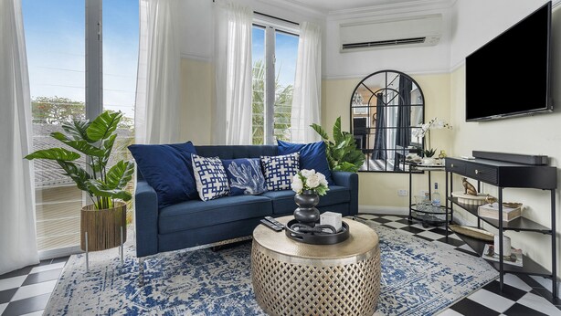 Un salon avec un canapé bleu, une table basse ronde et une grande fenêtre avec des rideaux.