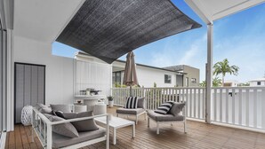 Un espace extérieur abrité doté d’une terrasse en bois, de mobilier blanc et d’un barbecue.