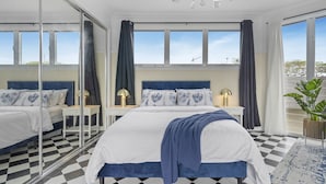 Une chambre avec un sol à carreaux, un grand lit recouvert d’un plaid bleu et un lustre.