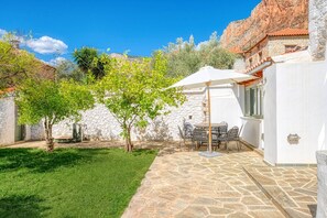 Un patio de piedra con una mesa y sillas, una pared blanca y un árbol.