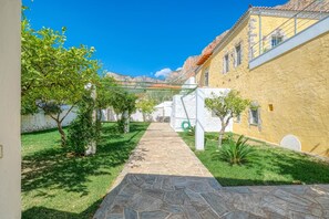 Un patio con un sendero de piedra que conduce a un edificio de fachada amarilla y pared blanca.