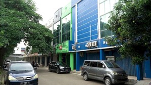 Un bâtiment à la façade bleue et verte, avec des voitures garées et des arbres.