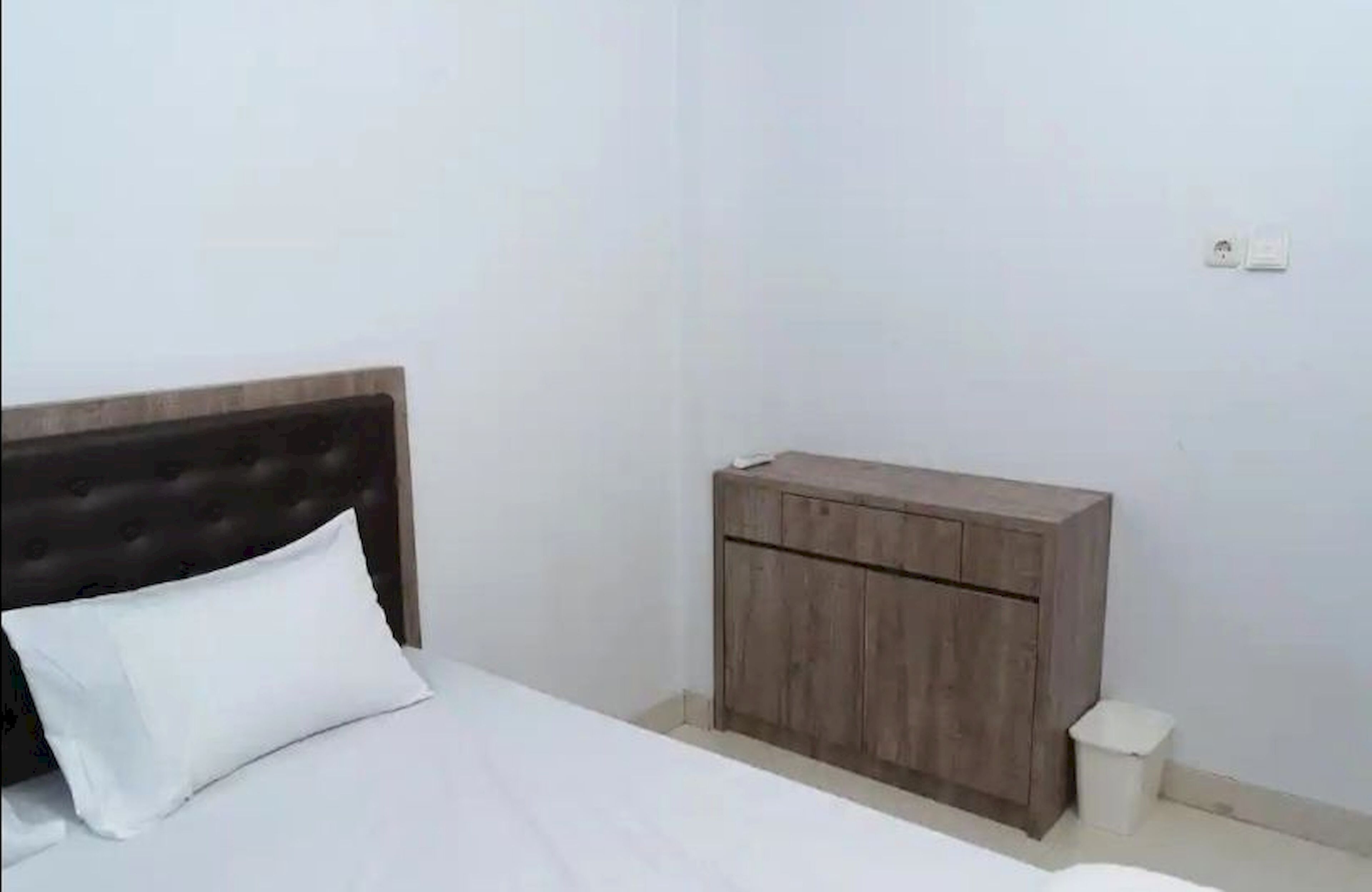 A bedroom with a bed, a wooden nightstand, and a small trash bin.