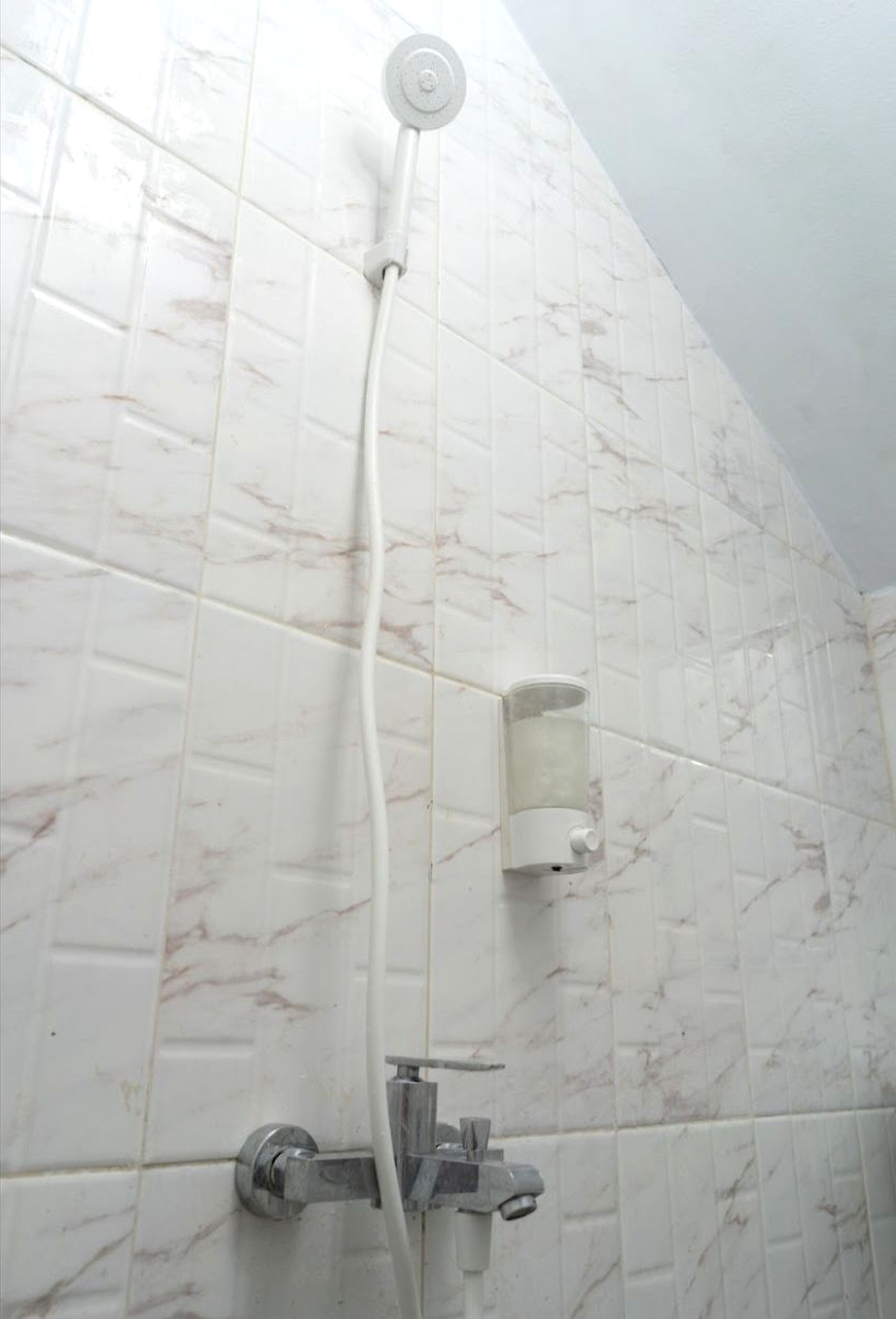 Ducha con cabezal de ducha de mano y dispensador de jabón empotrado en un baño con azulejos de mármol.