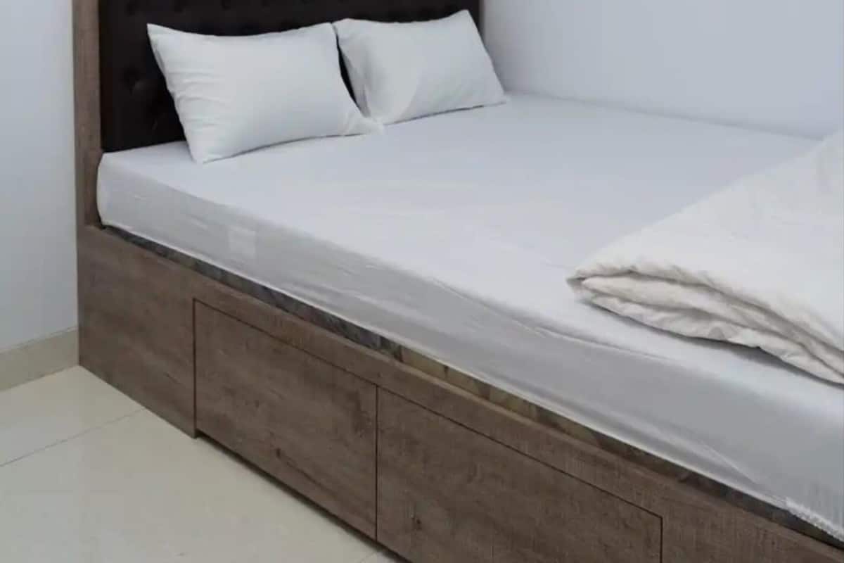 A single bed with a wooden headboard and two pillows, a wooden nightstand, and a white mattress.