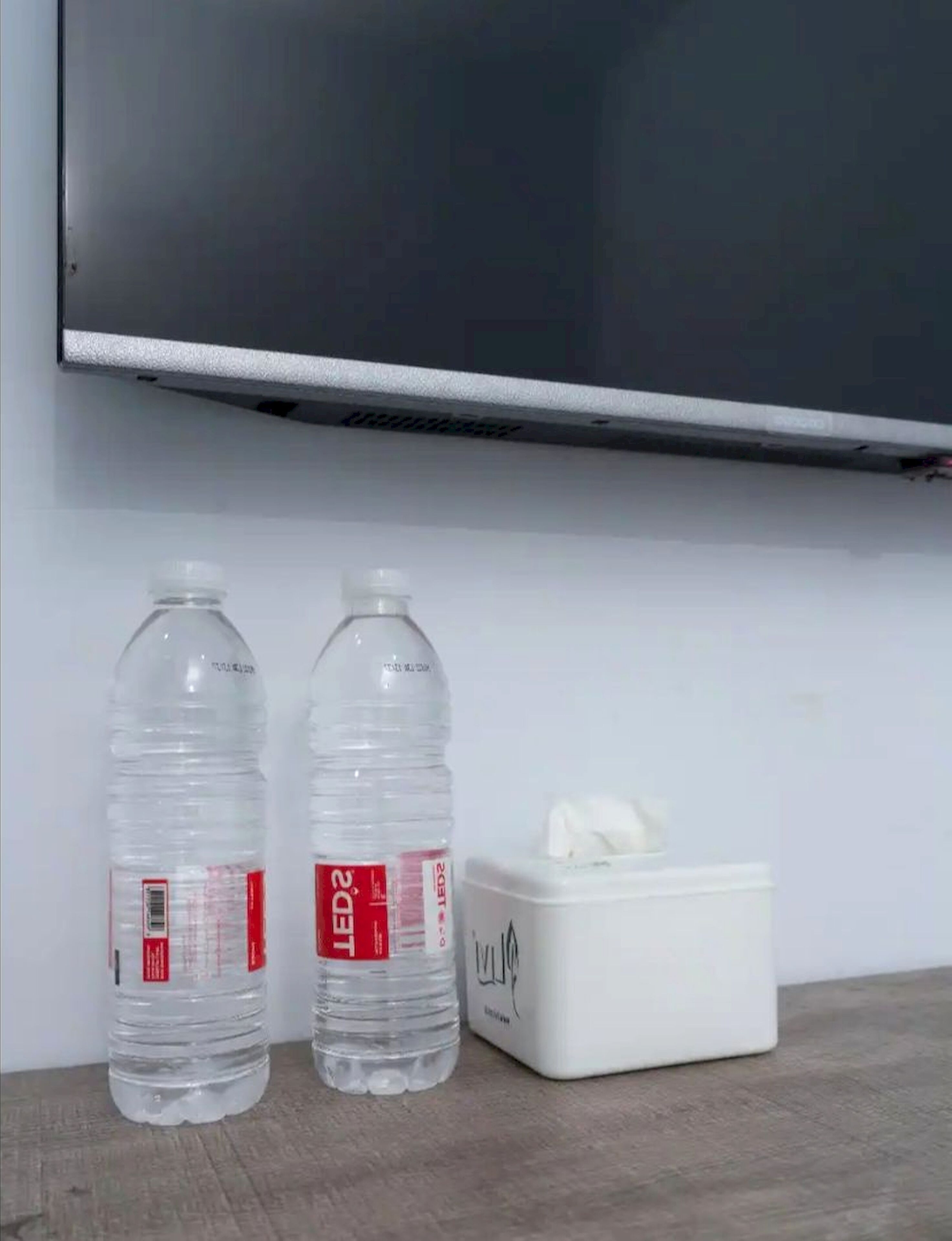 Two water bottles and a tissue box on a wooden surface against a white wall.