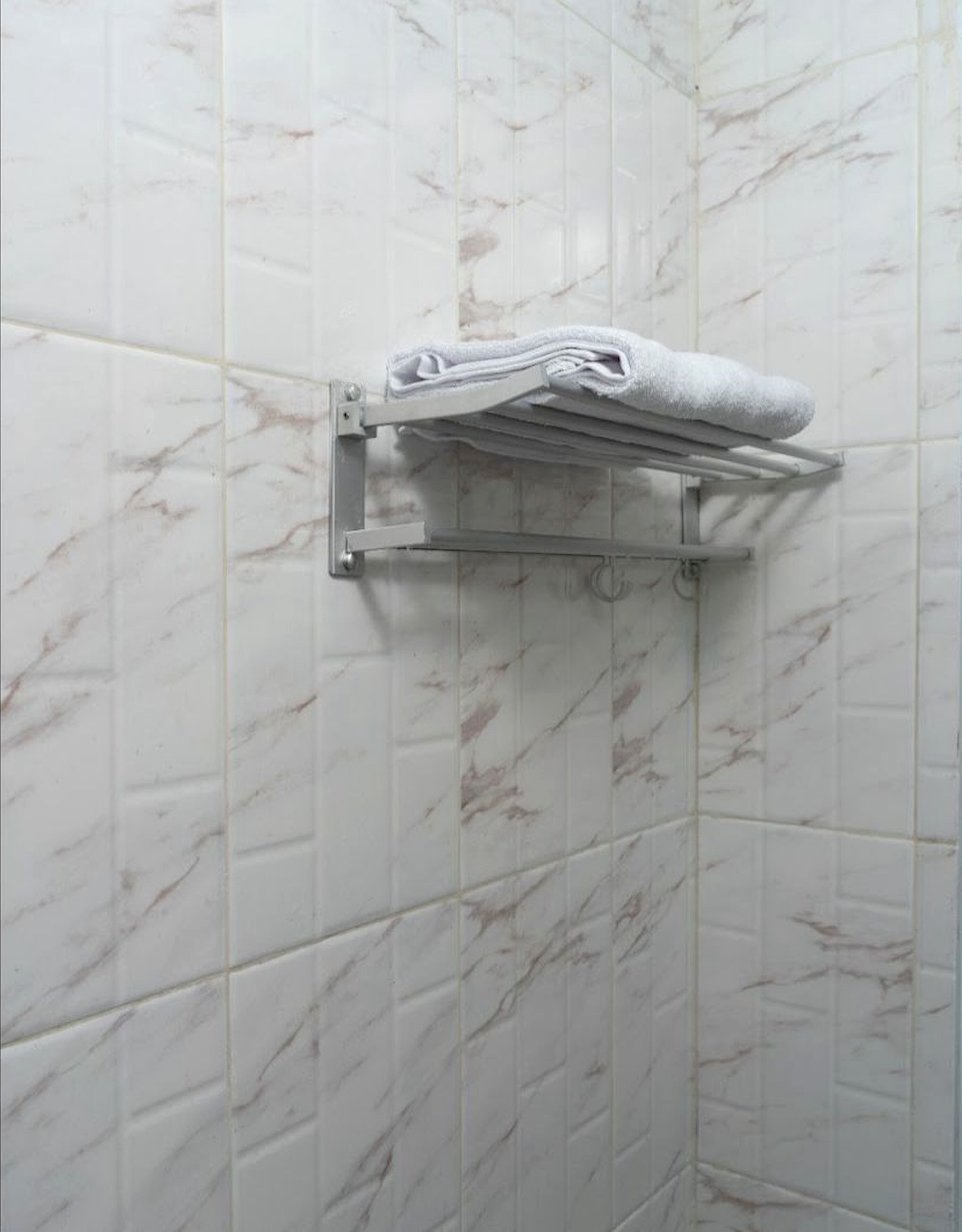 A bathroom with white marble tiles and a towel rack holding a folded towel.