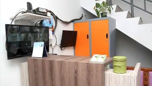 Un comptoir d’accueil avec un revêtement en bois, un écran plat, un petit écran numérique et une poubelle verte.