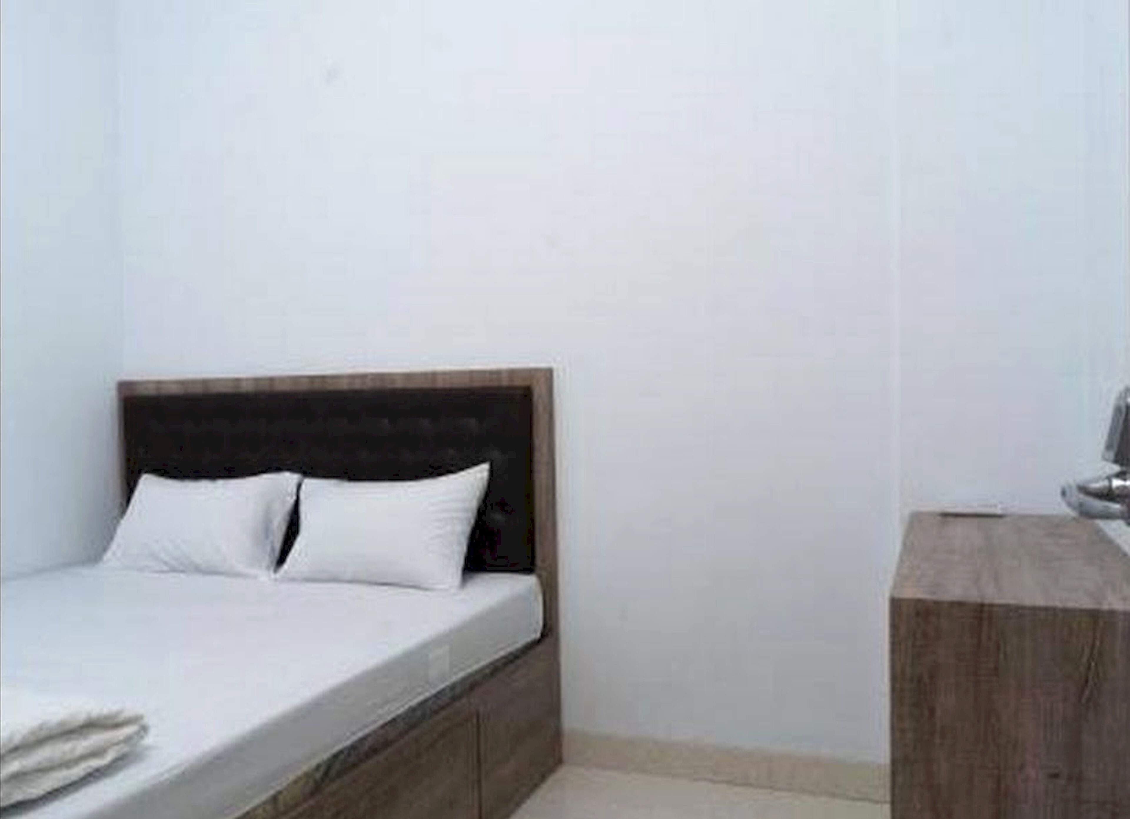 Un llit individual amb capçalera de fusta en una habitació amb parets blanques.