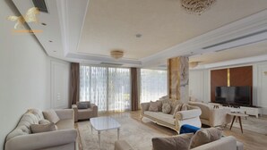 Ein geräumiges Wohnzimmer mit großem Fernseher, bequemen Sofas und einem Kronleuchter.