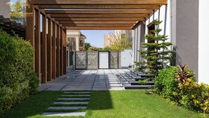 Ein überdachter Patio-Bereich mit einer Holz-Pergola, einem Steinpfad und gepflegtem Gras und Sträuchern.
