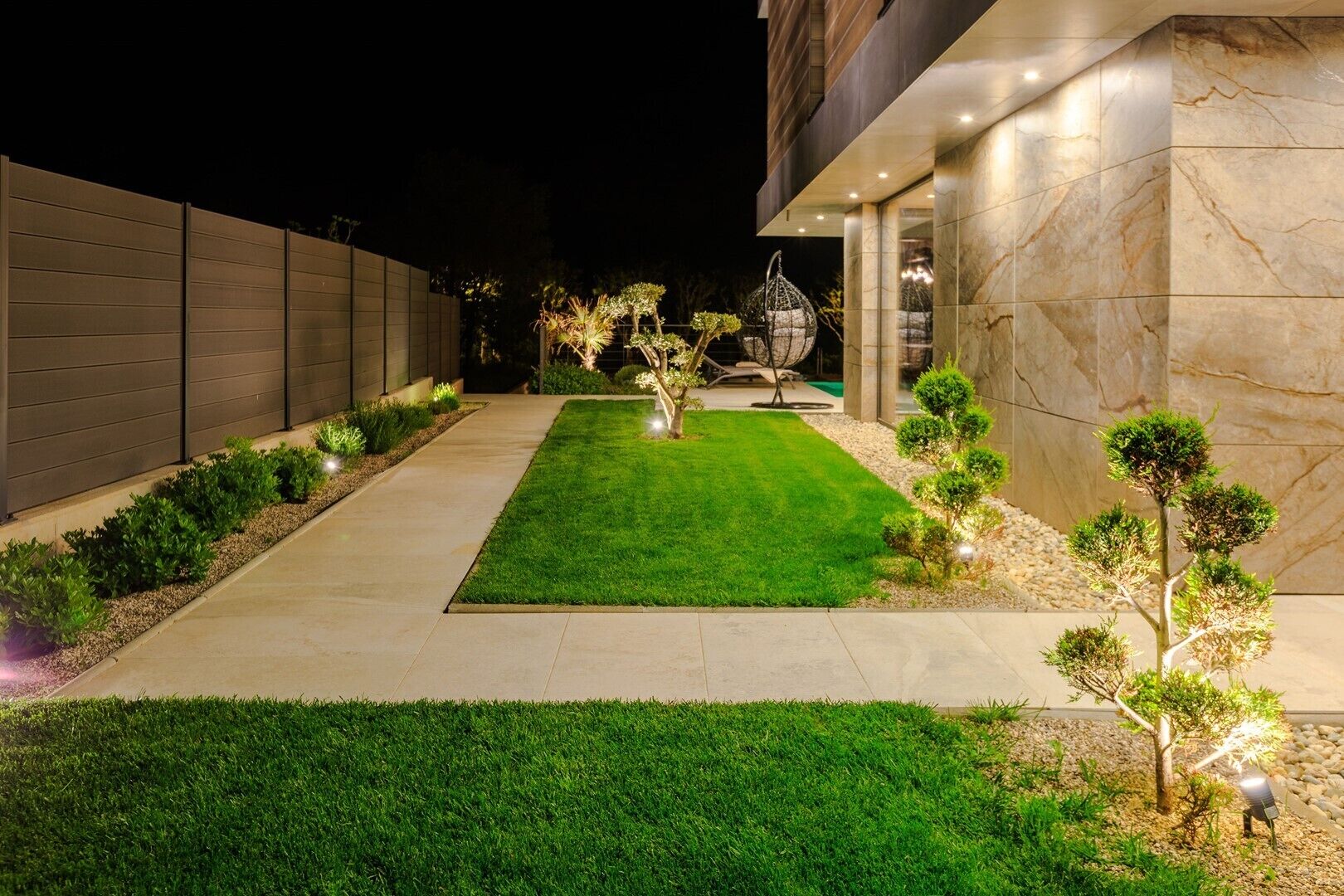 A modern building with a well-maintained lawn, decorative lighting, and a stone wall.