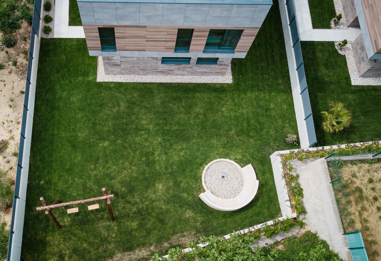 Luchtbeeld van een modern gebouw met een verzorgd gazon, een rond tuinelement en een houten schommel.