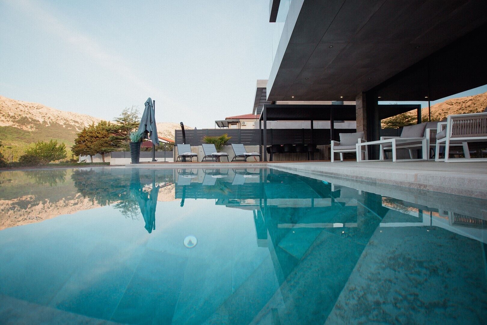 A modern pool area with clear water, lounge chairs, and a view of the surrounding landscape.