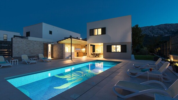 Une maison moderne dotée d’une piscine, d’un espace salon extérieur et offrant une vue sur les montagnes.