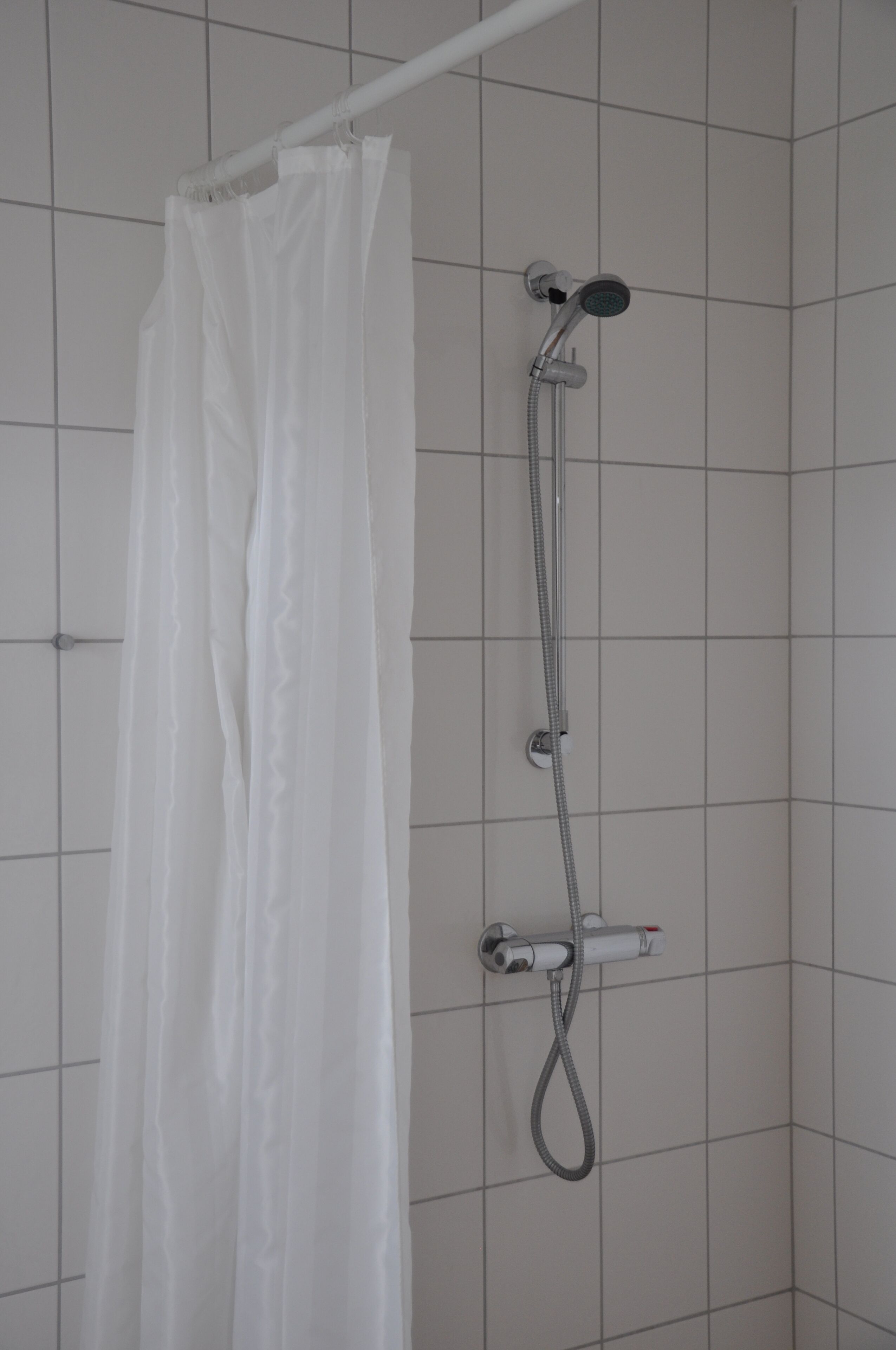 Une douche avec un rideau blanc et un pommeau de douche mobile.
