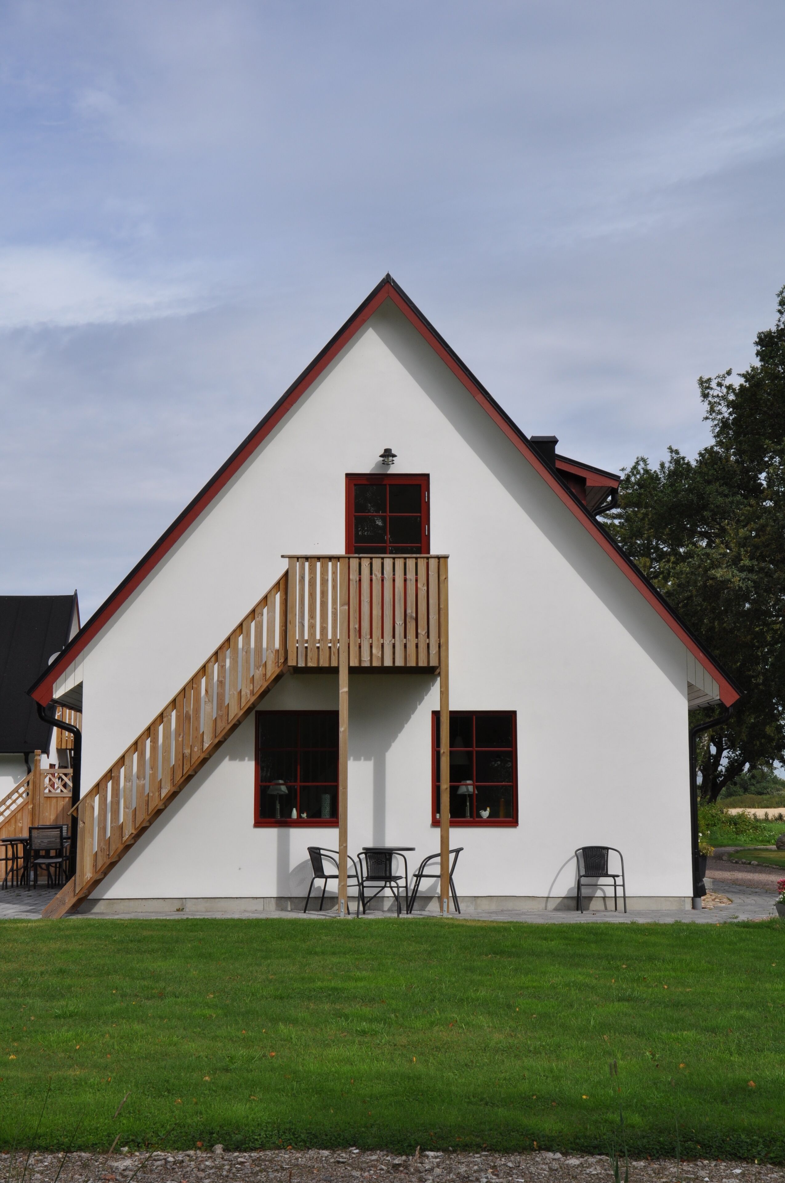 A white building with a red roof, a wooden staircase, and a balcony.