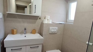 A compact bathroom with a white sink, mirror, and toilet. - Modern equipped apartment in the  center of Baška, near the sea (Baska)