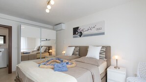A modern bedroom with a large bed, bedside tables, a chair, and a wall-mounted air conditioner.