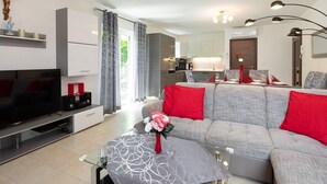 A modern living room with a grey sofa, red cushions, a glass coffee table, and a flat-screen TV.