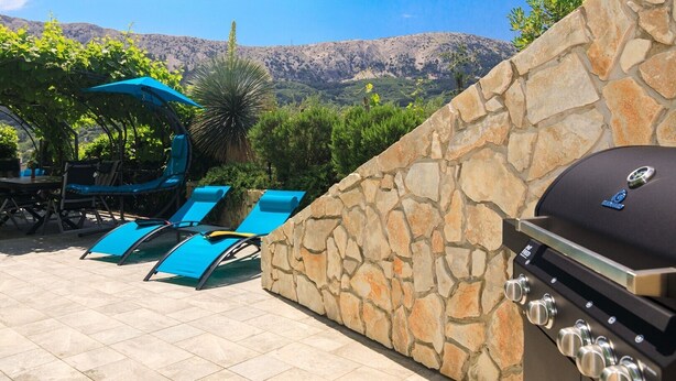 An outdoor patio with stone walls, a grill, and blue lounge chairs.