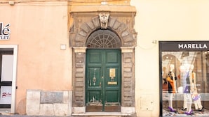 La façade d’un immeuble avec une porte verte, une fenêtre où sont exposés des mannequins et une enseigne indiquant « MARELLA ».