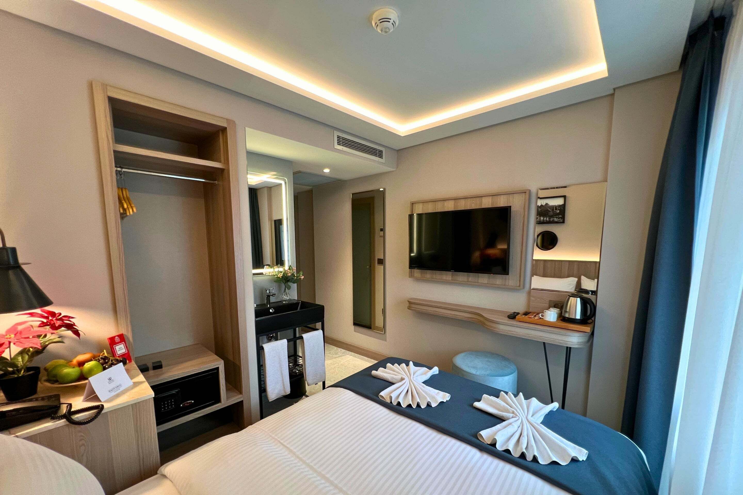 Une chambre d’hôtel comprenant un lit, un bureau avec une lampe, une coiffeuse avec un miroir, une télévision et une salle de bain avec douche.