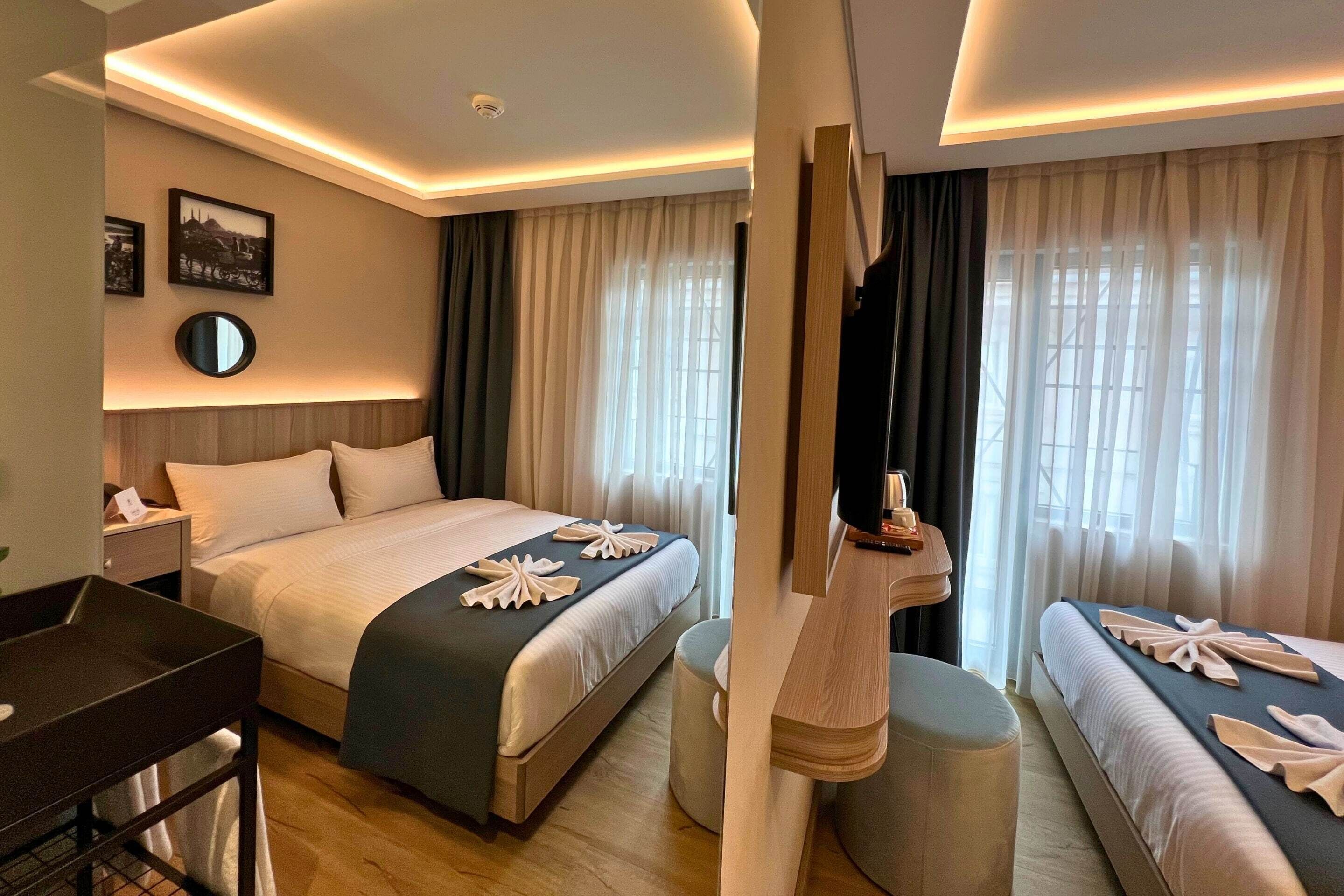 Una habitación de hotel con una cama grande, una cama más pequeña, un escritorio y un espejo.