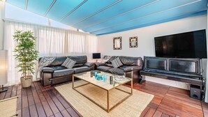 Ein Wohnzimmer mit einem Glastisch, zwei Ledersofas, einem großen Flachbildfernseher und einer Bambuspflanze.
