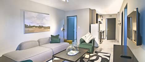 A modern living room with a sofa, a coffee table, and a green armchair. There is a door leading to another room.