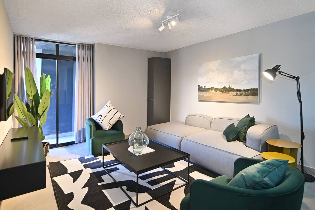 Een moderne woonkamer met een bank, fauteuils, een salontafel en een groot raam met gordijnen.