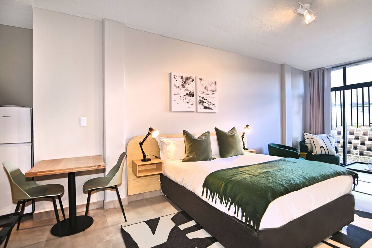 Een moderne hotelkamer met een bed, een bureau, stoelen, een klein tafeltje en kunst aan de muur.