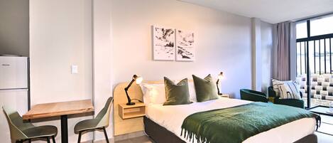 Een moderne hotelkamer met een bed, een bureau, stoelen, een klein tafeltje en kunst aan de muur.